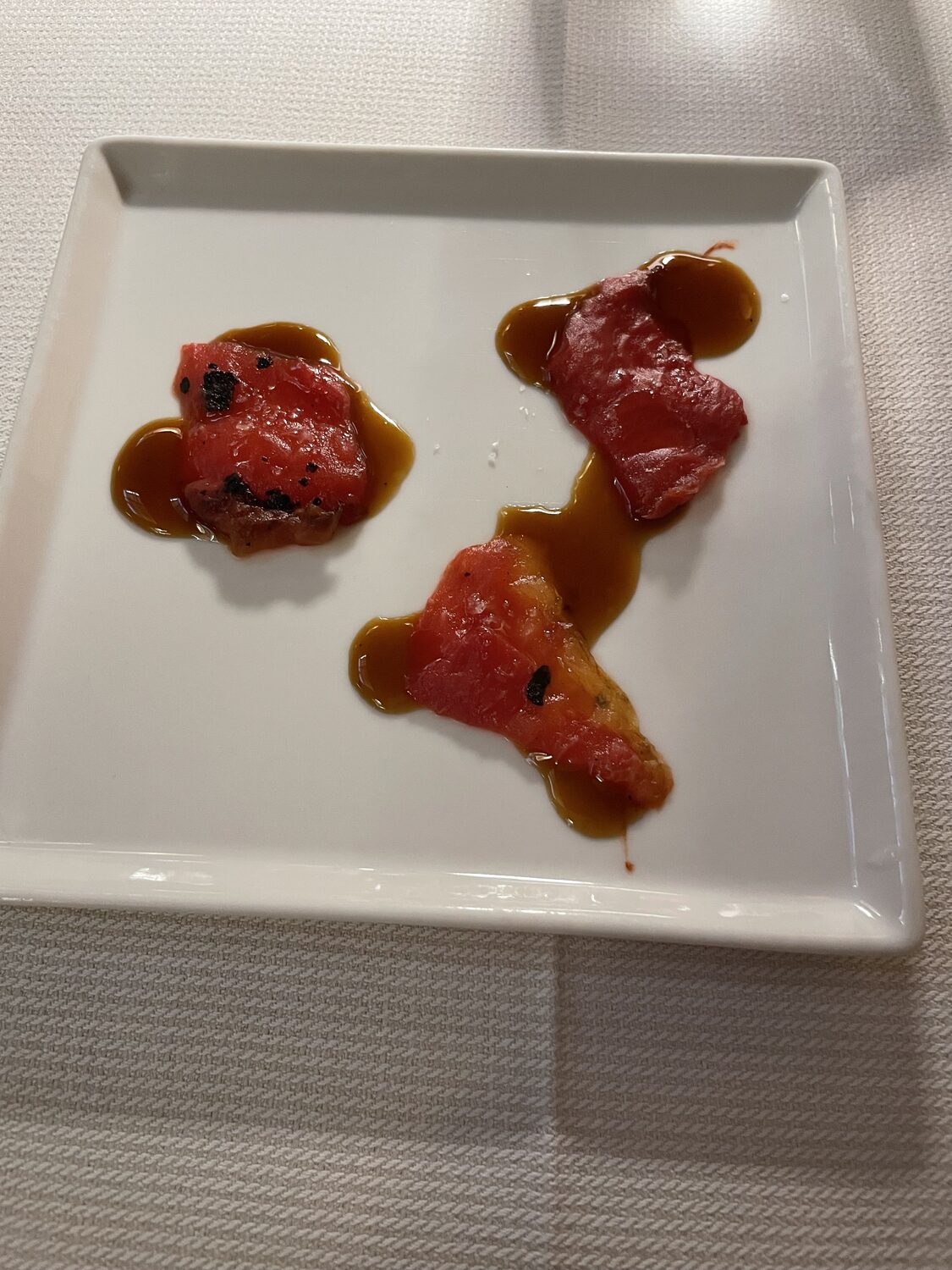 Piccoli bocconi rossi con salsa su un piatto quadrato bianco