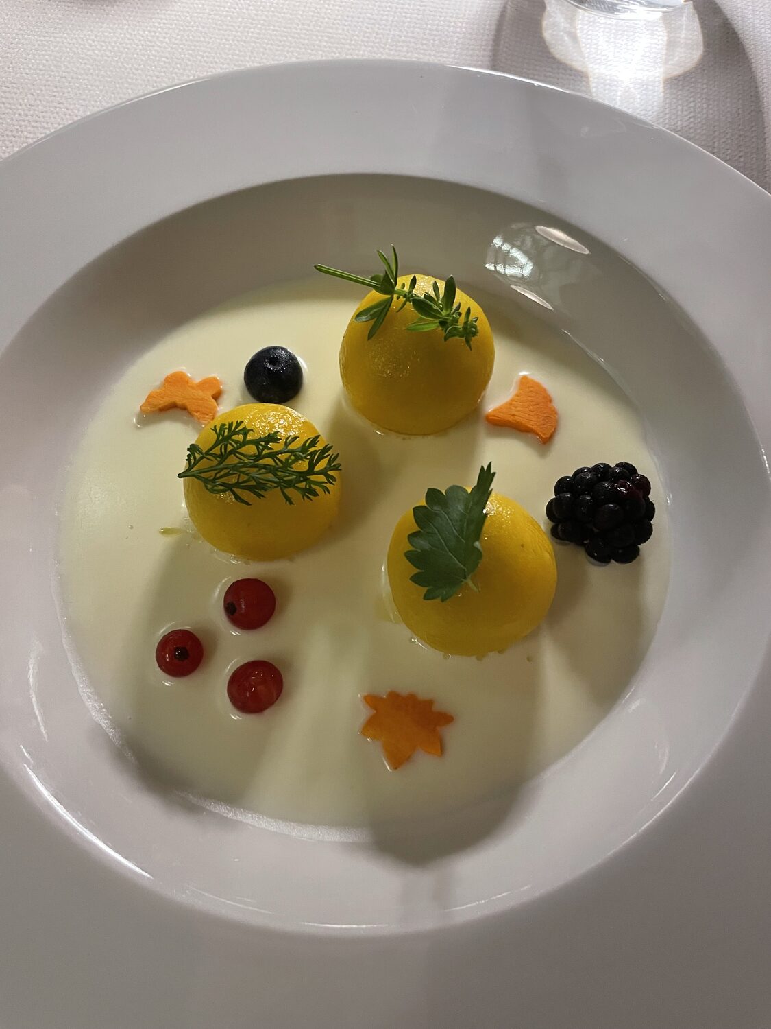 Sfere gialle in una crema chiara, decorate con erbe e piccoli frutti