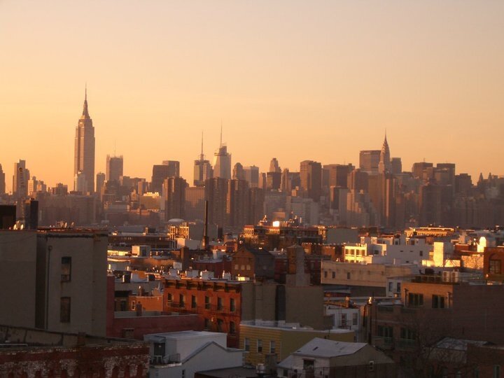 The Manhattan skyline at sunset, with the Empire State and the Chrysler, seen beyond the rooftops